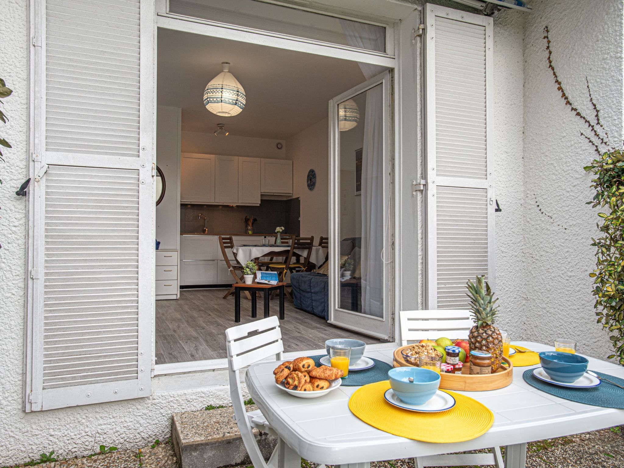 Eine offene Terrasse mit Esstisch, gedeckt für ein Frühstück, mit Croissants, Obst und einer Ananas.
