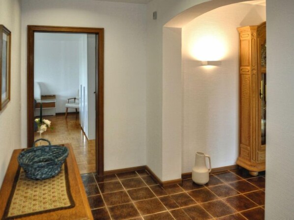 A hallway with a wooden floor, a white wall, and a door leading to another room.