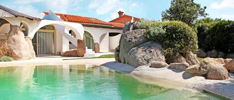 Una villa moderna con piscina, grandes rocas y techo de tejas rojas.