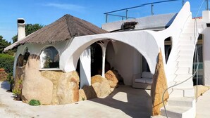Una casa moderna con un diseño arquitectónico único, destacando una fachada de piedra, ventanas arqueadas y un tejado de paja.