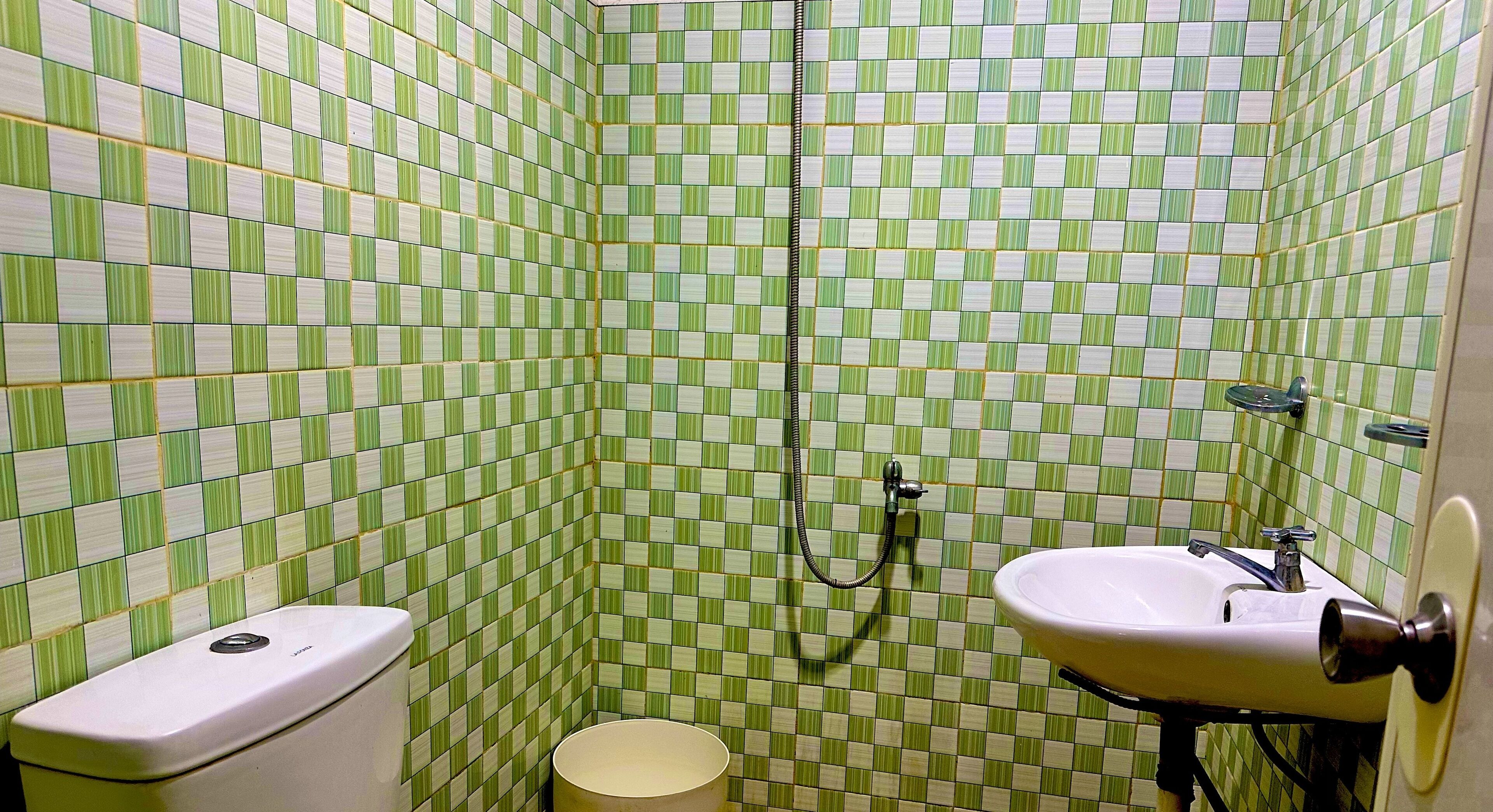 Uma casa de banho com padrão de azulejos verde e branco em xadrez, um toalete, uma pia e um chuveiro.