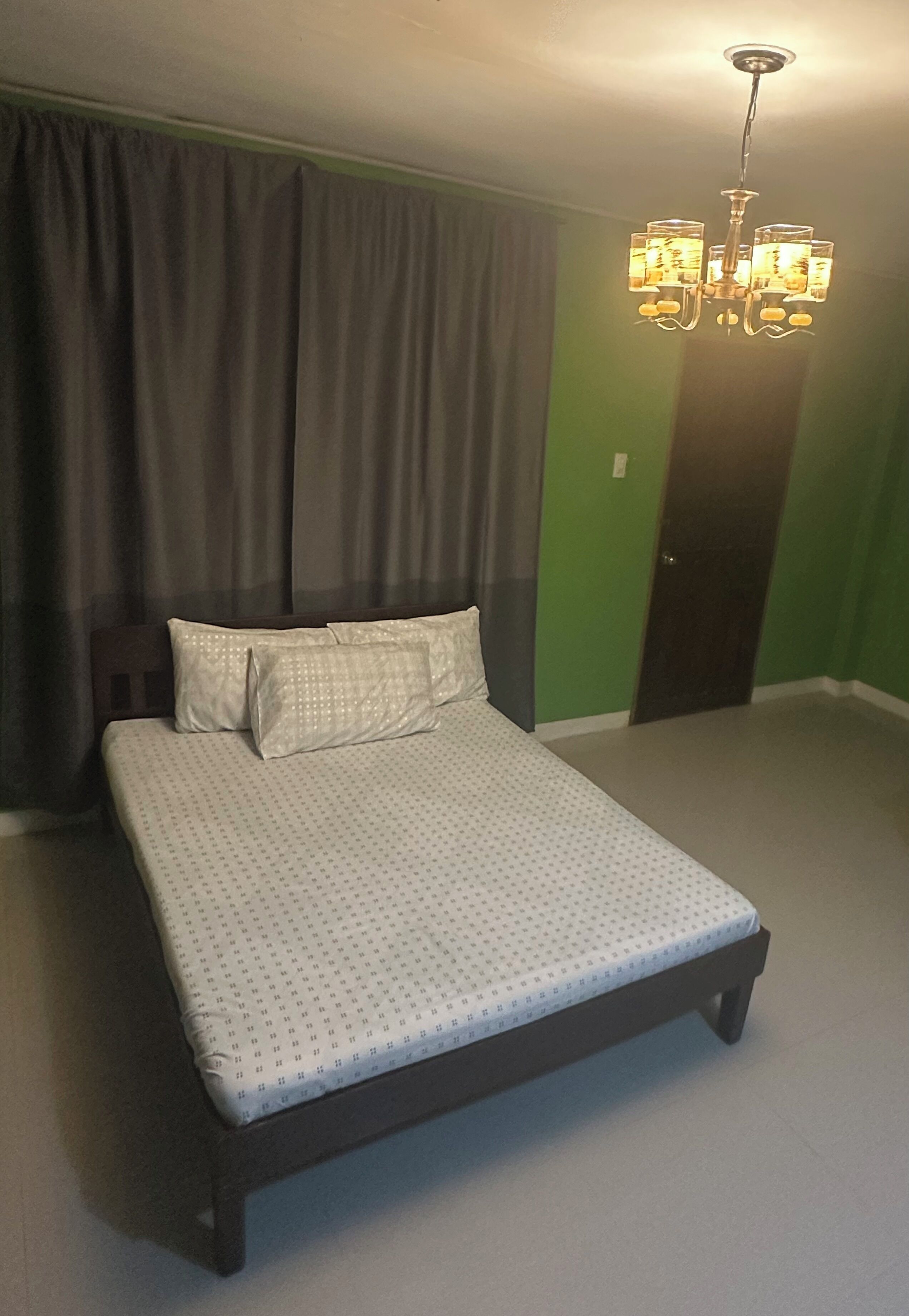 A bedroom with a bed, curtains, a chandelier, and a green wall.