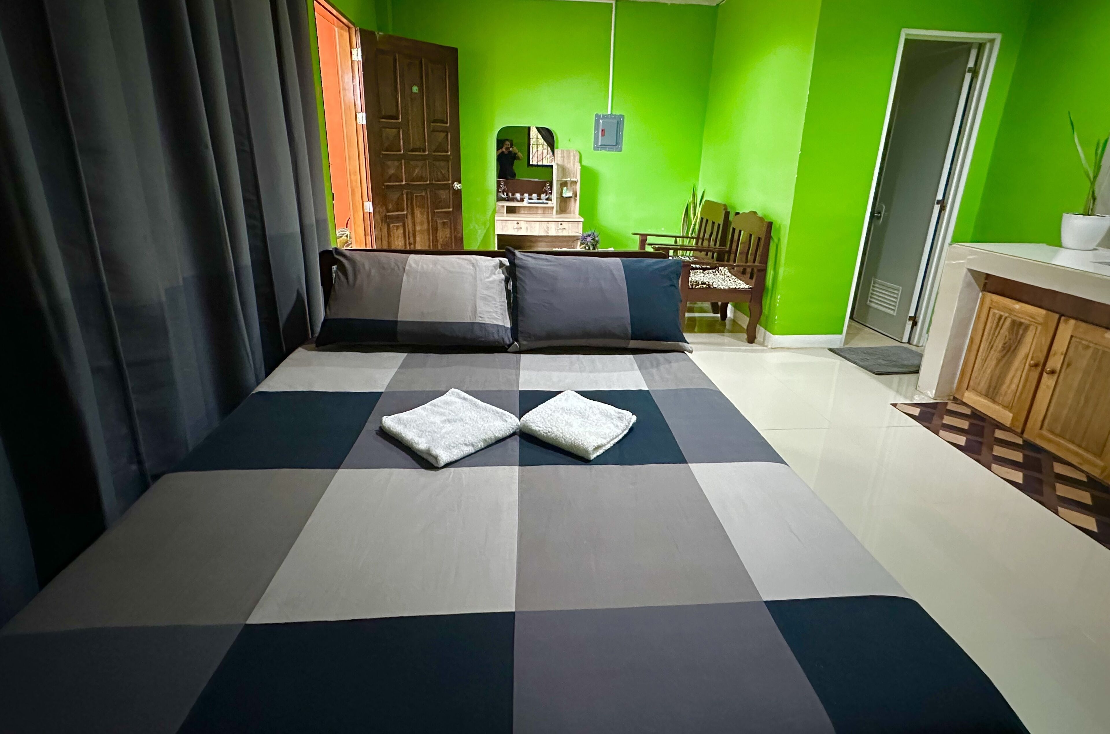 A room with a checkered floor, a bed with pillows, a wooden wardrobe, and a green wall.