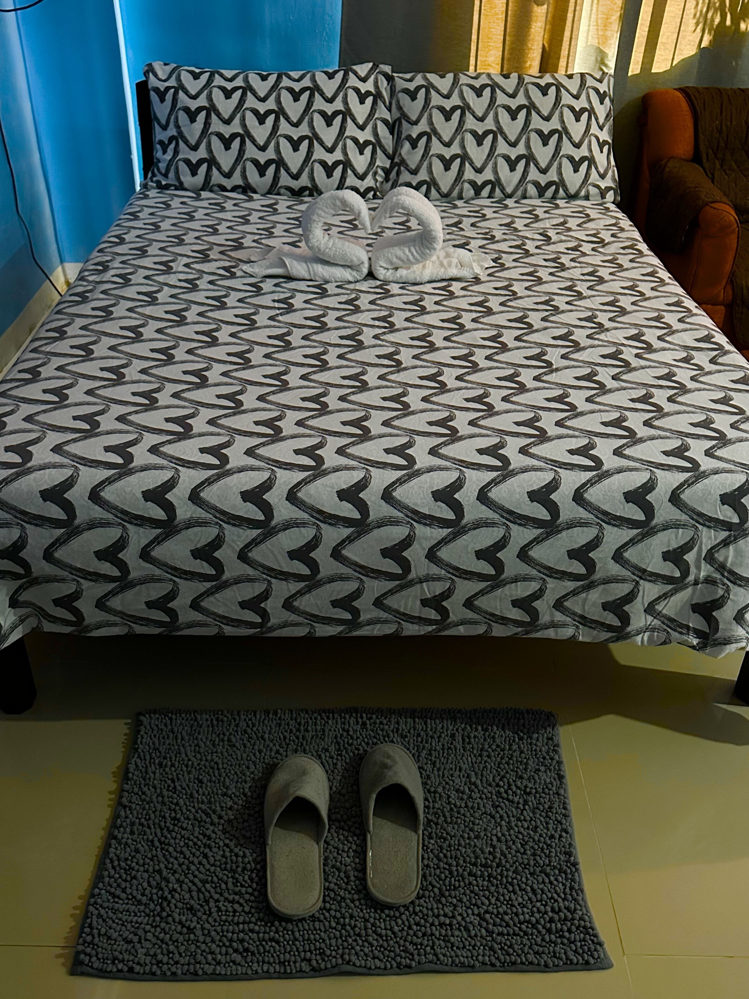 A bed with a patterned bedspread, heart-shaped pillows, and a pair of shoes on a rug.