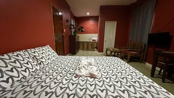 Habitación de hotel con una cama grande, una mesa de comedor, un televisor y una kitchenette al fondo.