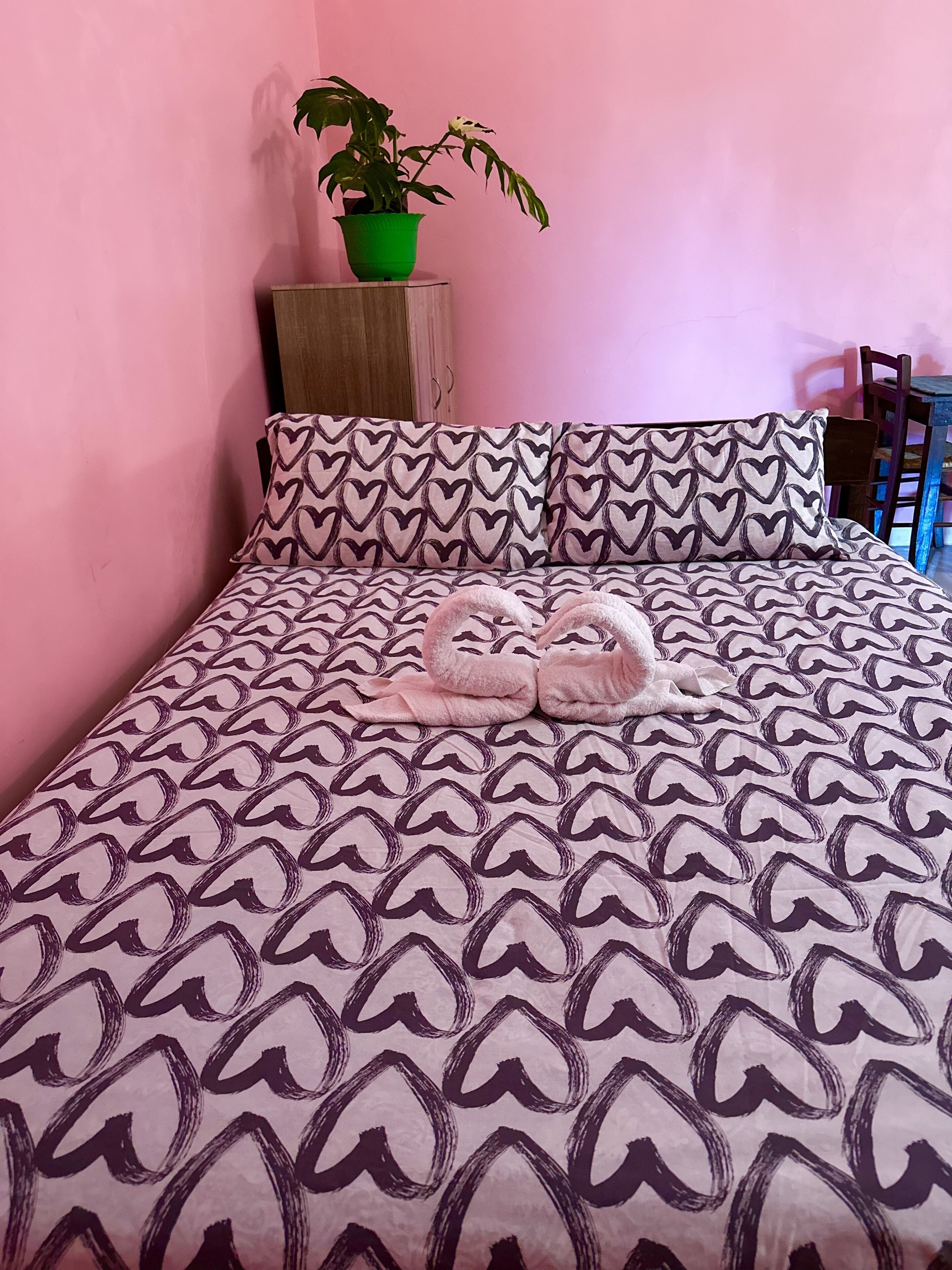 A bed with a patterned bedspread, a green potted plant, and heart-shaped pillows.