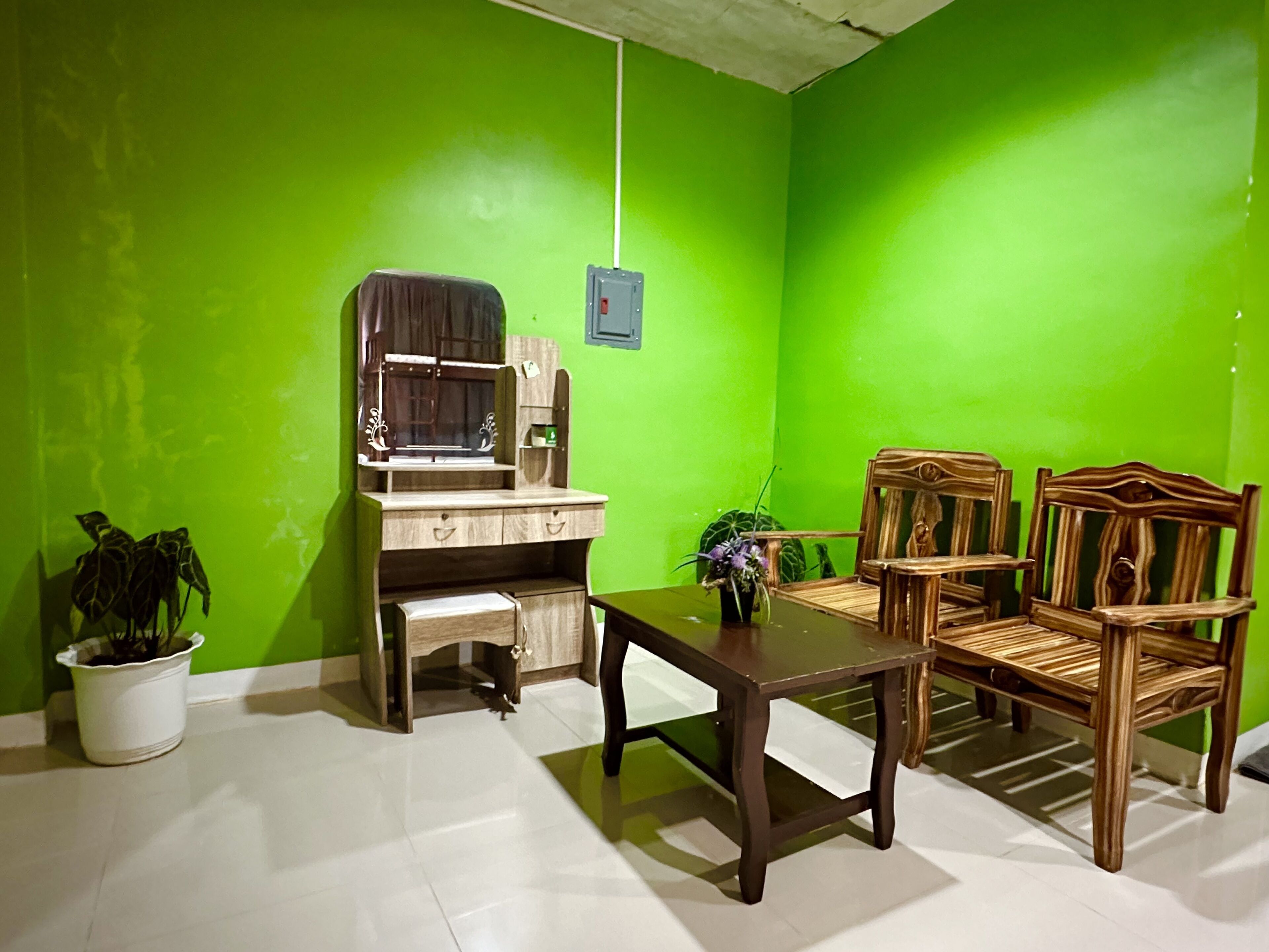A room with a green wall, a wooden desk with a chair, a small table, and two wooden chairs.