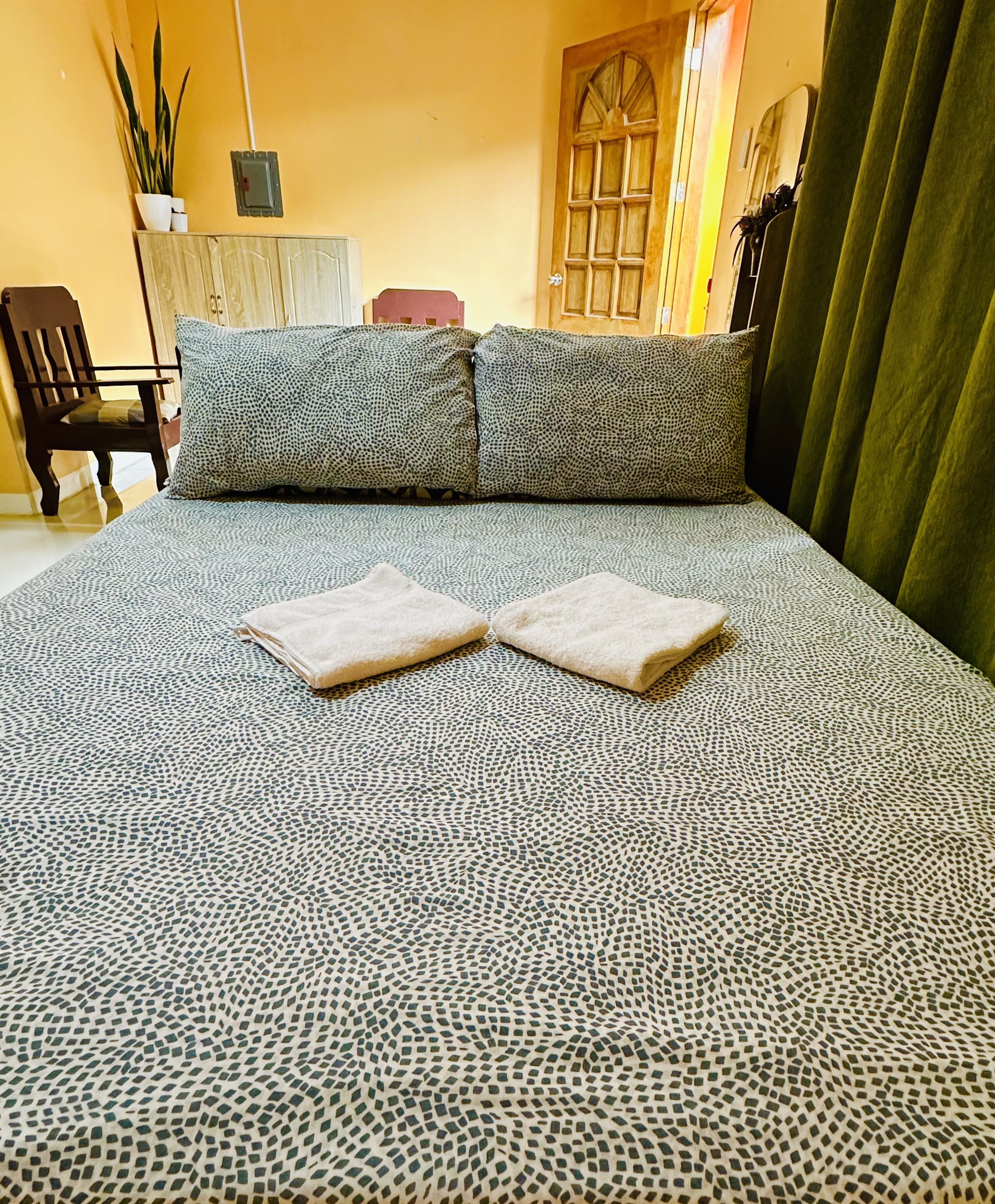 A neatly made bed with a patterned bedspread, two pillows, and two folded towels.