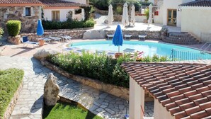 A pool area with lounge chairs and umbrellas, surrounded by stone buildings with tiled roofs.