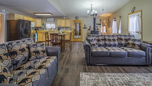 A spacious living room with a large sofa and a dining area with wooden cabinets and a refrigerator.