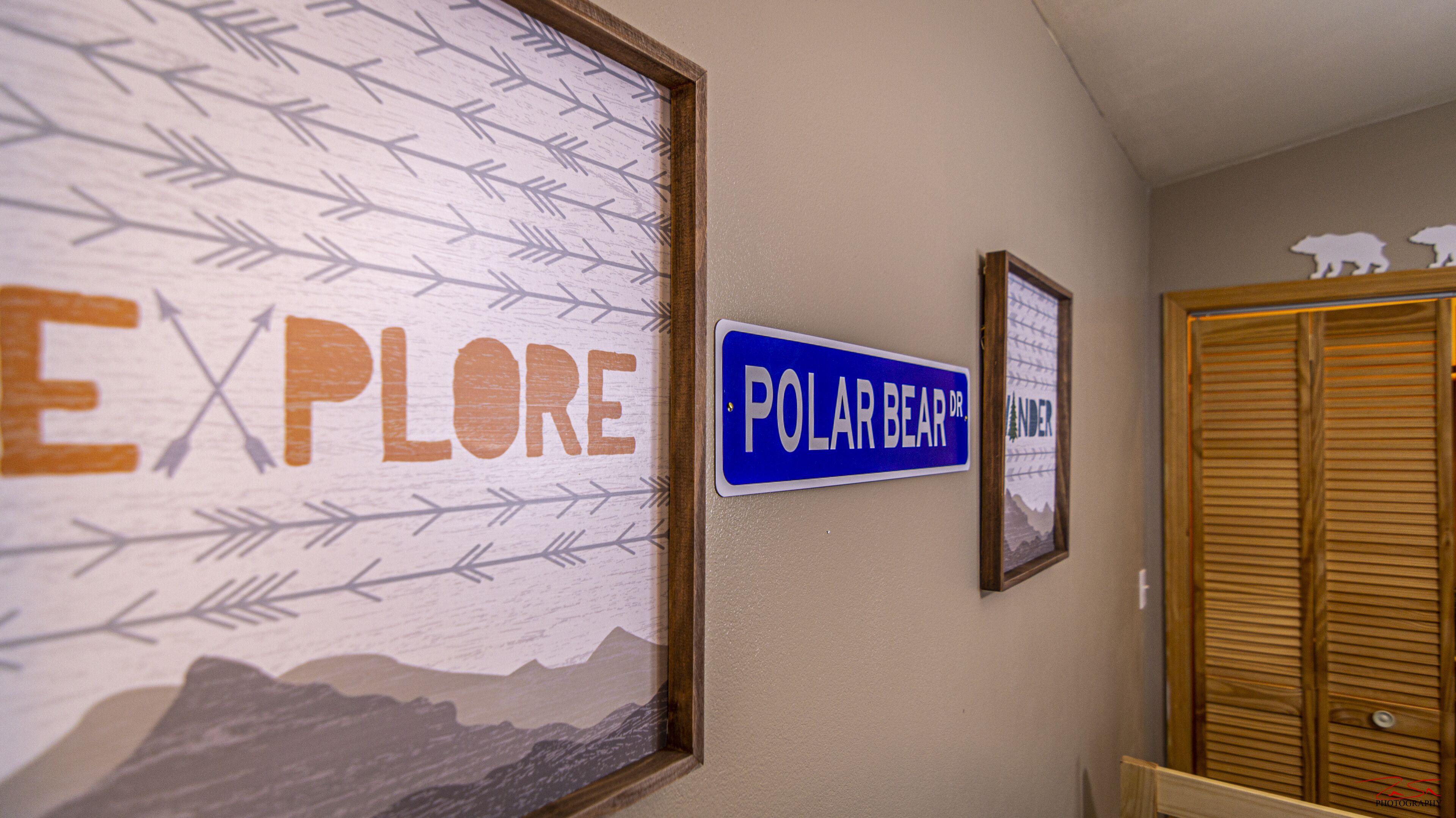 Ein Flur mit einer Wand, die mit einem Schild 'Explore' und einem Schild 'Polar Bear Dr' verziert ist. Es befinden sich gerahmte Bilder und eine Holztür dort.