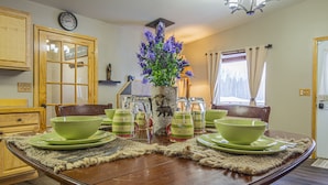 A dining table set with green plates, bowls, and cups, a vase with purple flowers, and a wooden cabinet in the background.