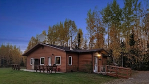 A wooden cabin with a satellite dish, a porch, and a picnic table.