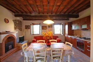 A dining area with a table set for four, surrounded by wooden chairs, a brick fireplace, and a stone wall. - House in Camaiore center for 5 People with Garden (Camaiore)