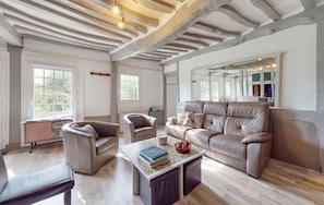 A spacious living room with a high ceiling, large windows, a leather sofa, and a coffee table with books and apples. - Homerez - House in Vittefleur, garden. (Vittefleur)