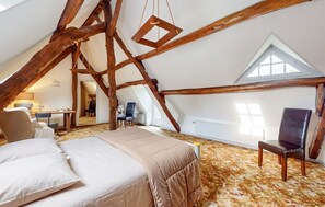 A bedroom with a sloped ceiling, exposed wooden beams, a bed, a chair, and a desk with a lamp. - Homerez - House in Vittefleur, garden. (Vittefleur)