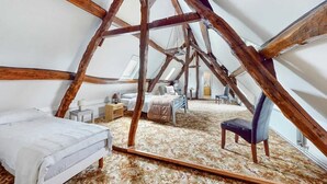 Ein Schlafzimmer mit schrägen Wänden, Holzbalken, einem Bett, einem Sessel und einem kleinen Tisch.
