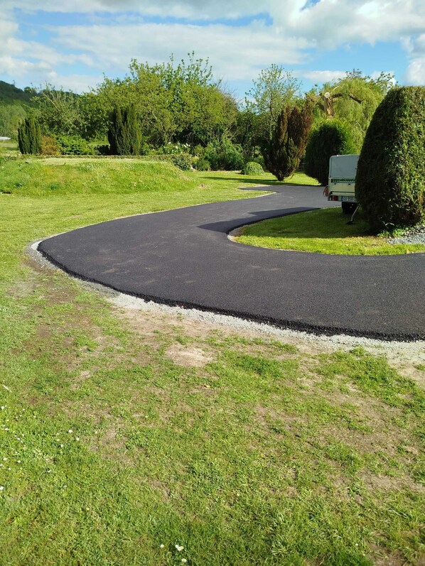 A winding paved path in a grassy area with a vehicle parked nearby. - Homerez - House in Vittefleur, garden. (Vittefleur)