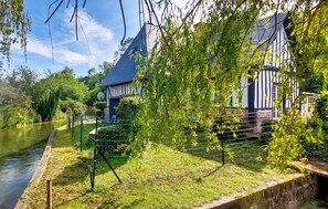 A traditional building with a sloped roof, surrounded by lush greenery and a body of water.