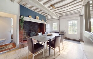 A dining area with a stone fireplace, a white ceiling with exposed beams, and a view of the outdoors through a window. - Homerez - House in Vittefleur, garden. (Vittefleur)