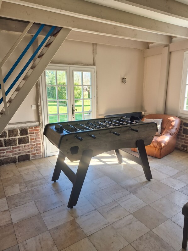 A foosball table in a room with a brick wall, a window, and a brown leather chair. - Homerez - House in Vittefleur, garden. (Vittefleur)