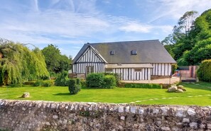 A traditional half-timbered house with a sloped roof, surrounded by a well-maintained lawn and mature trees. - Homerez - House in Vittefleur, garden. (Vittefleur)