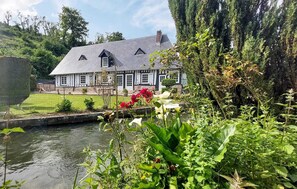 A traditional house with a sloped roof, a small garden, and a pond in the foreground. - Homerez - House in Vittefleur, garden. (Vittefleur)