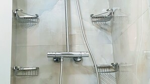 A shower with a handheld showerhead, a wall-mounted faucet, and two chrome towel racks.