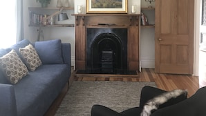 A living room with a fireplace, a blue sofa, a black armchair, and a wooden door. - Bryce Cottage by Webb hotels (Leamington)