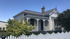 A two-story house with a white picket fence, a porch with decorative trim, and a chimney. - Bryce Cottage by Webb hotels (Leamington)