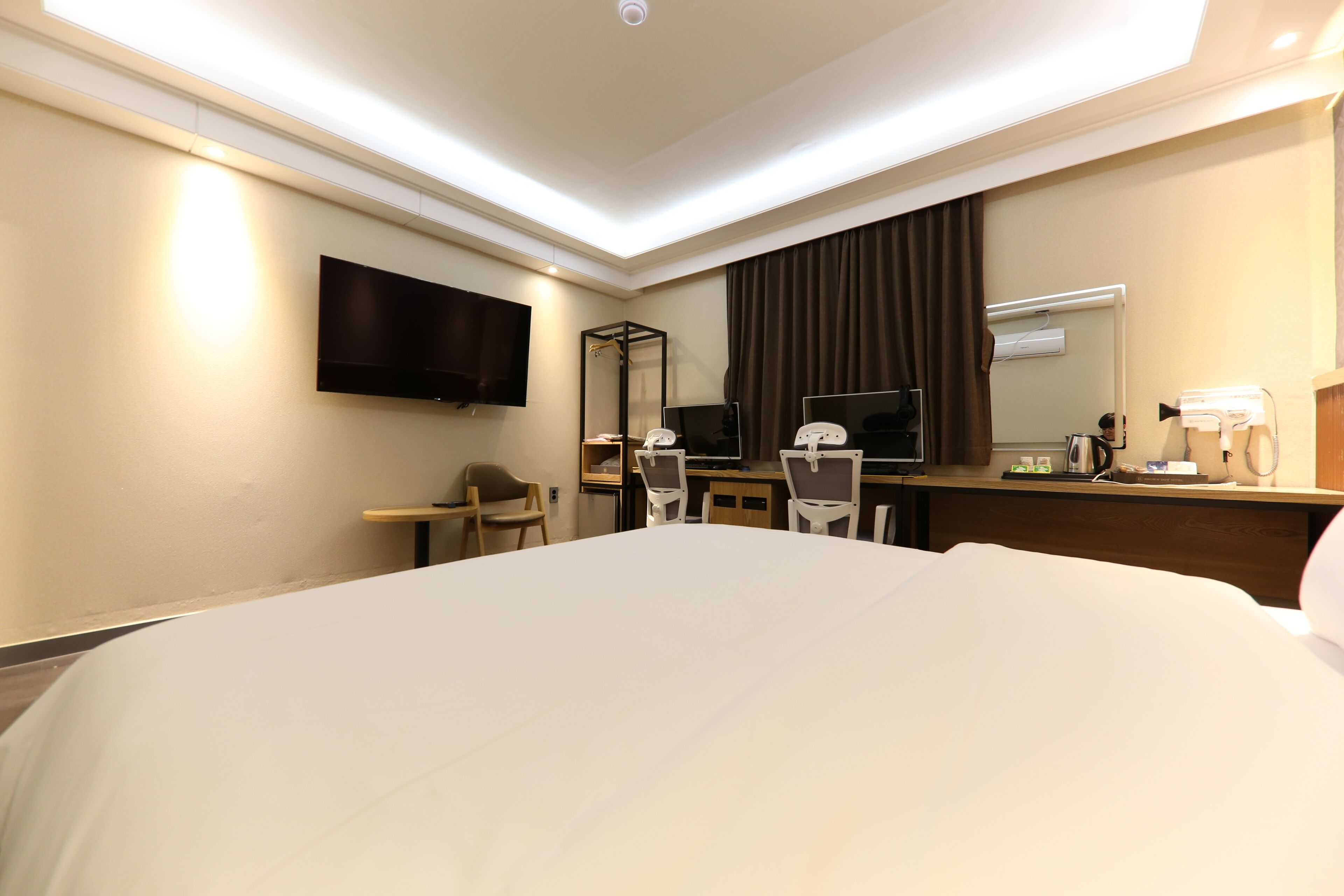Habitación de hotel con una cama grande, un escritorio con silla, un televisor de pantalla plana montado en la pared, un espejo y una ventana con cortinas.