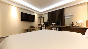 Habitación de hotel con una cama grande, un escritorio con silla, un televisor de pantalla plana montado en la pared, un espejo y una ventana con cortinas.