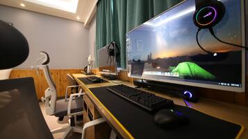 A computer desk with a monitor, keyboard, headphones, and a microphone.