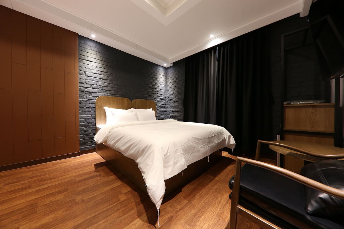 A modern bedroom with a wooden bed, a black brick accent wall, and a dark curtain.