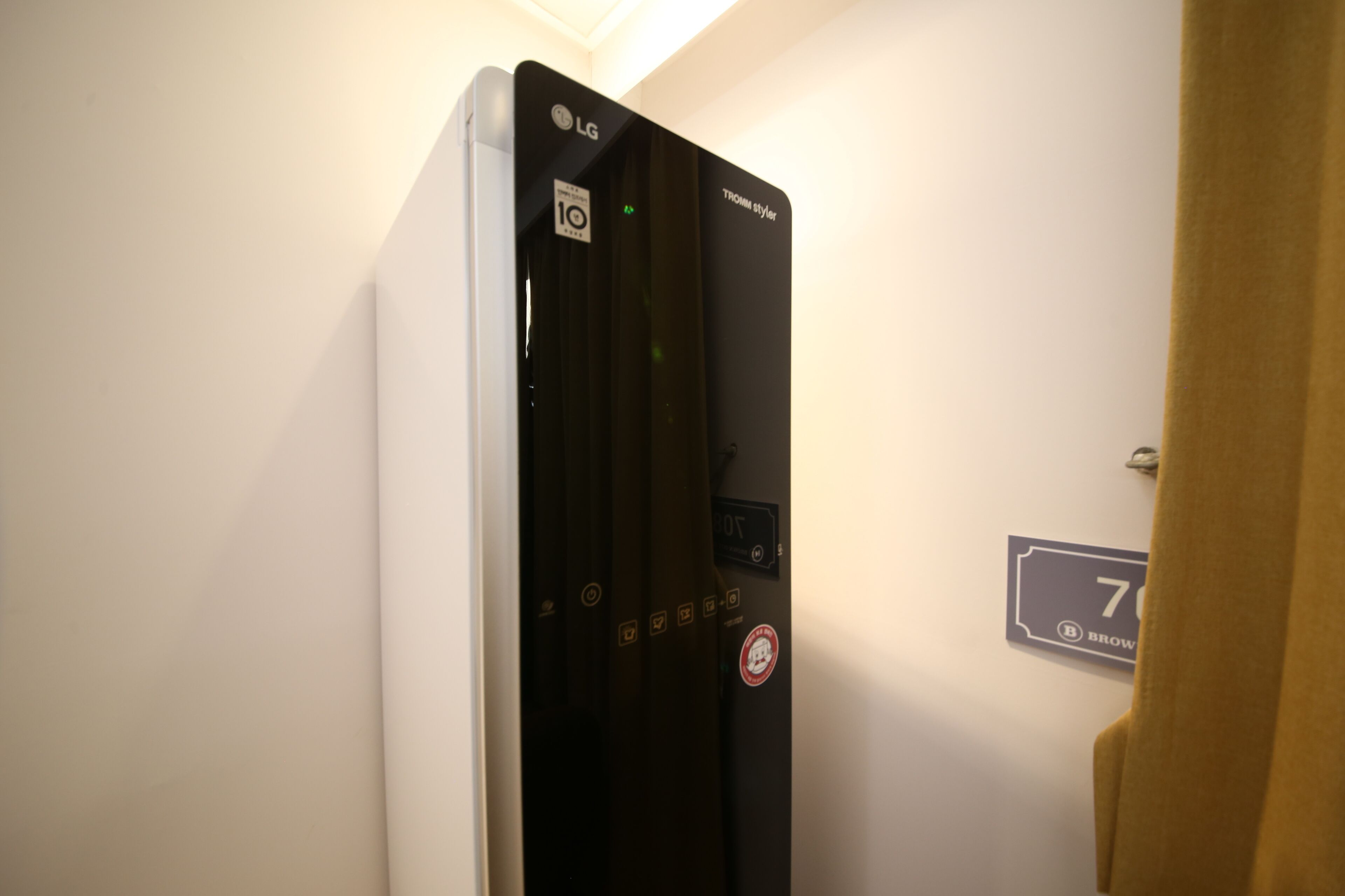 Um termostato preto da LG fixado numa parede branca, com uma placa de número de porta '7' e um indicador de temperatura '10'.