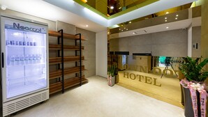 A hotel reception area with a Neocool branded refrigerator, wooden shelving, and a reception desk with a 'BLOW N'DOX HOTEL' sign. - Brown Dot Hotel Cheonan (Cheonan)