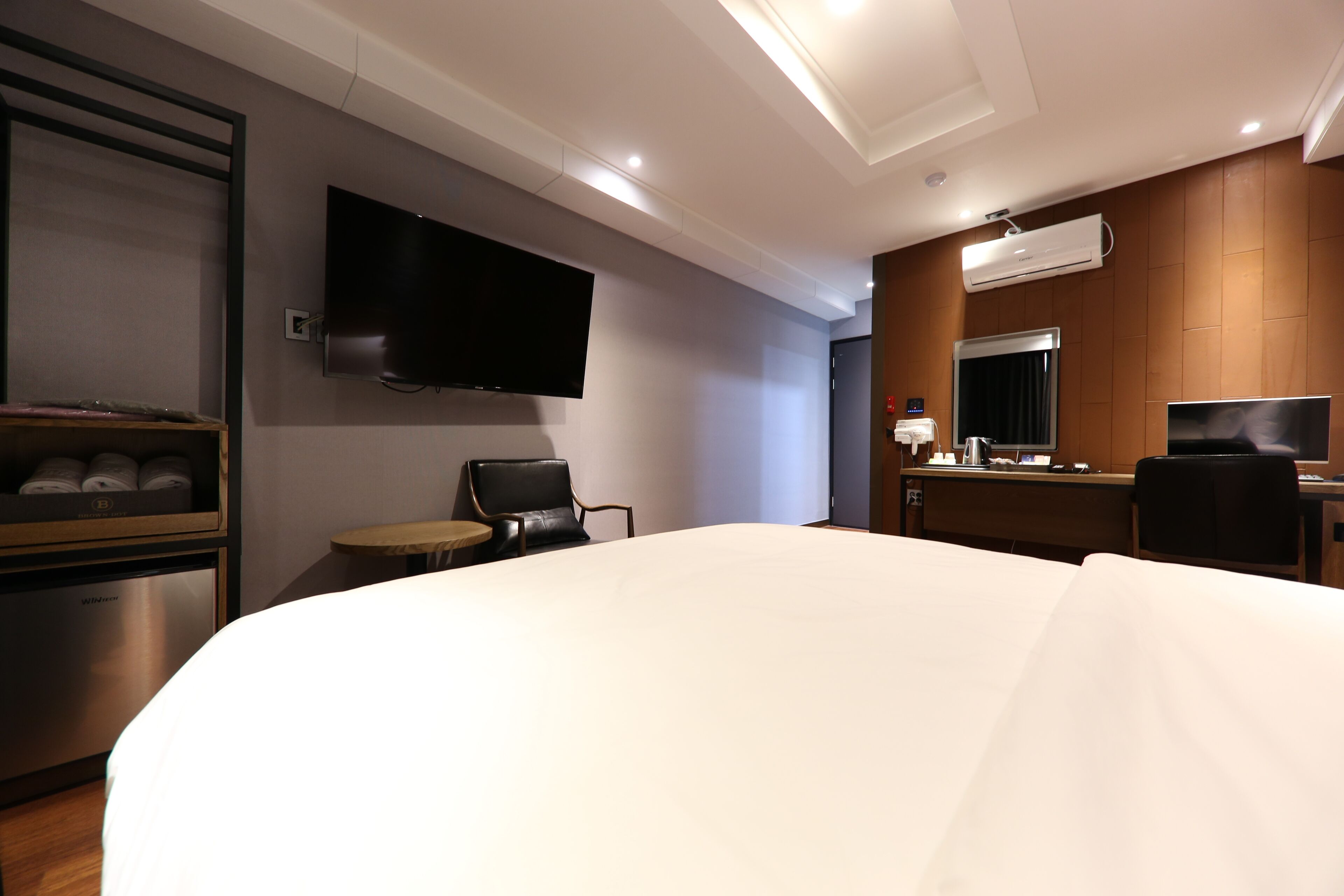 A hotel room with a large bed, a flat-screen TV mounted on the wall, a desk with a chair, and a minibar.