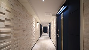 A long, narrow hallway with a light-colored brick wall on one side and a dark blue wall on the other. The floor is light wood, and the hallway is well-lit with ceiling lights. - Brown Dot Hotel Cheonan (Cheonan)