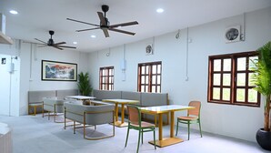 A modern interior with ceiling fans, a sofa, tables, chairs, and a potted plant.