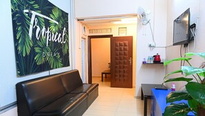 A modern living room with a black leather sofa, a wall-mounted TV, a door with a geometric pattern, and a small table with a red kettle and bottles.
