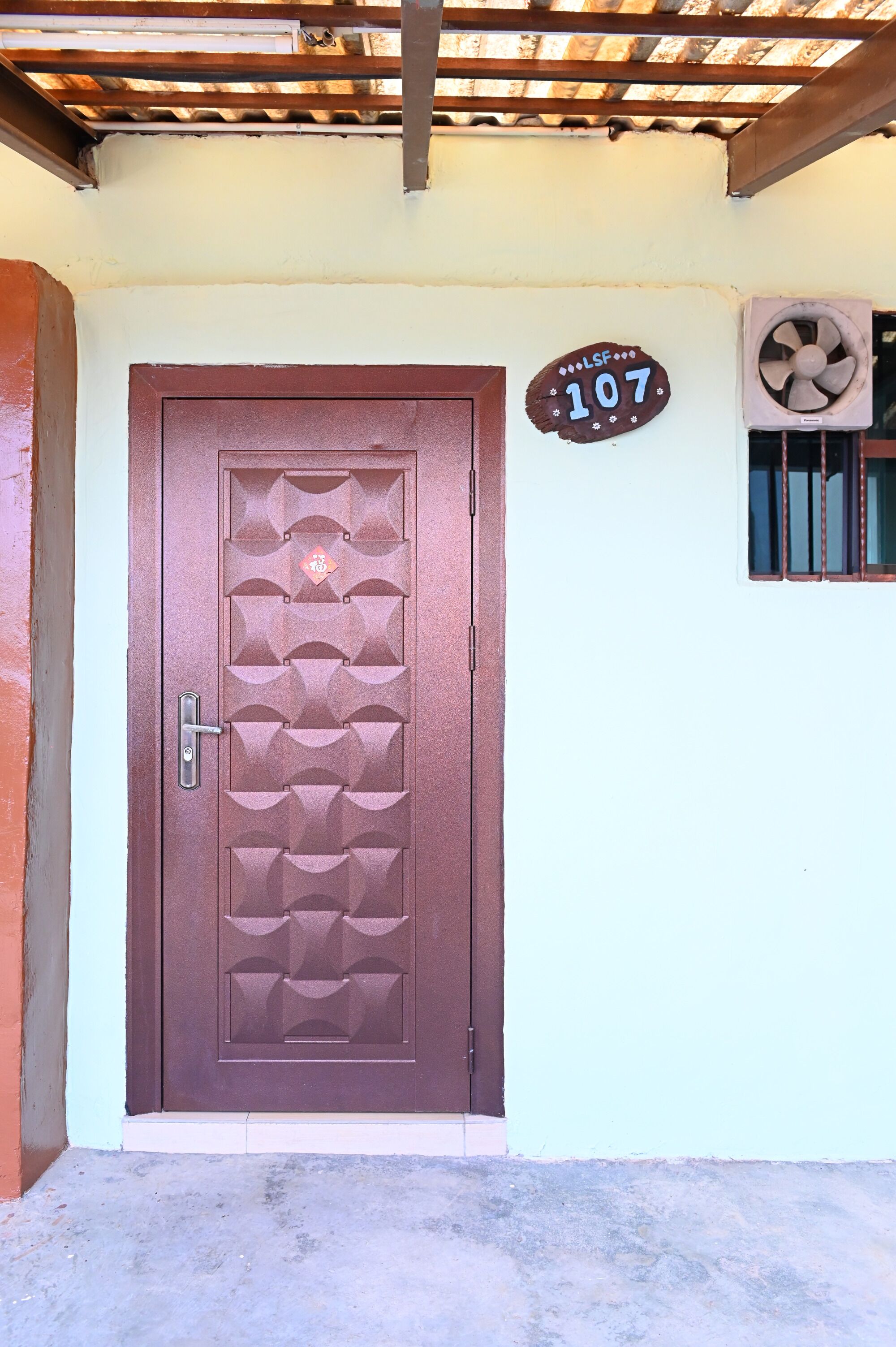A brown door with a decorative pattern, a number sign '107' on the wall, and a window with bars.