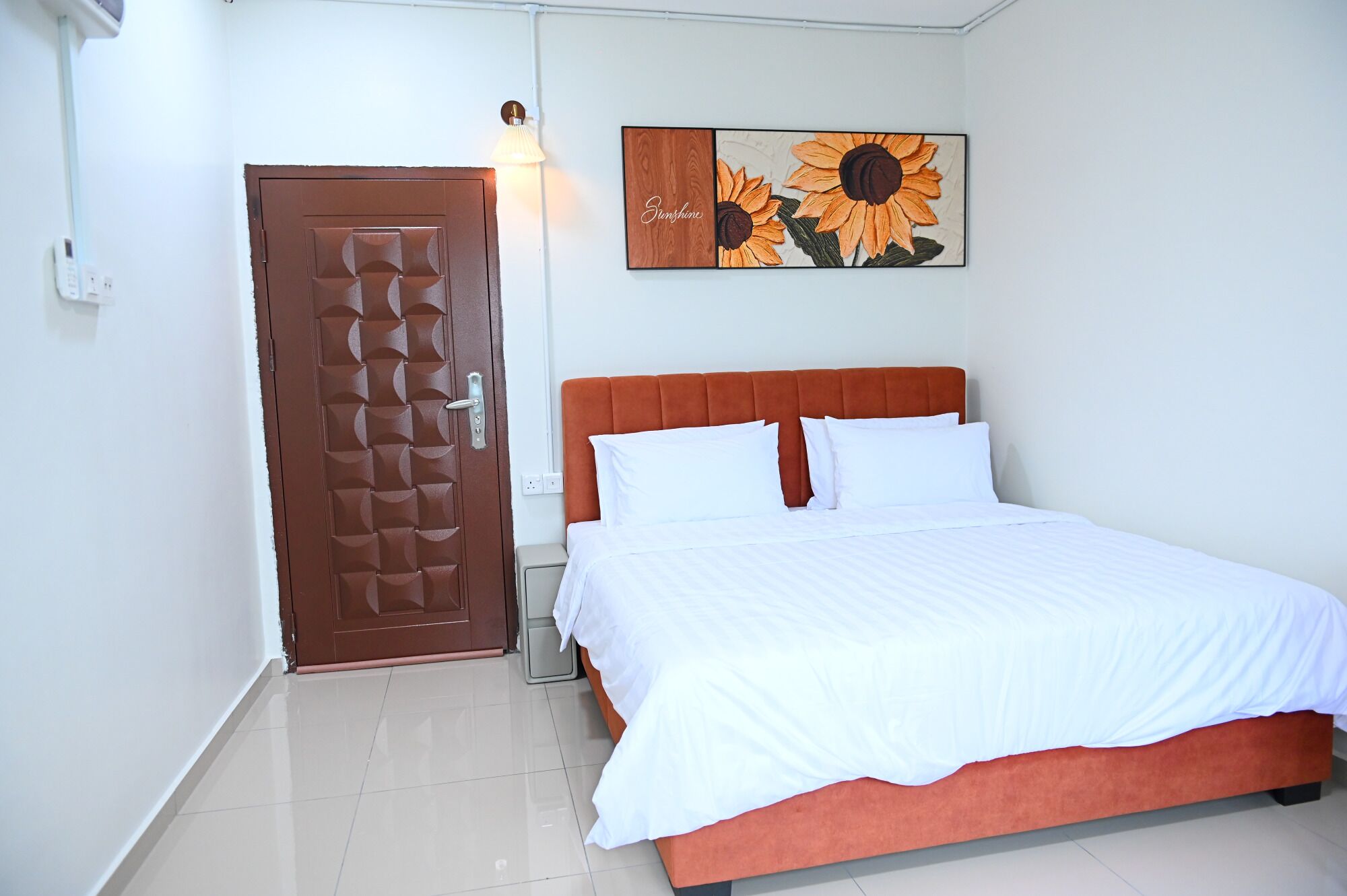 Un dormitorio con cama, una puerta, una lámpara de pared y un cuadro.