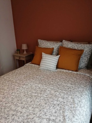 A bed with floral bedding, two orange pillows, and a bedside table with a lamp.