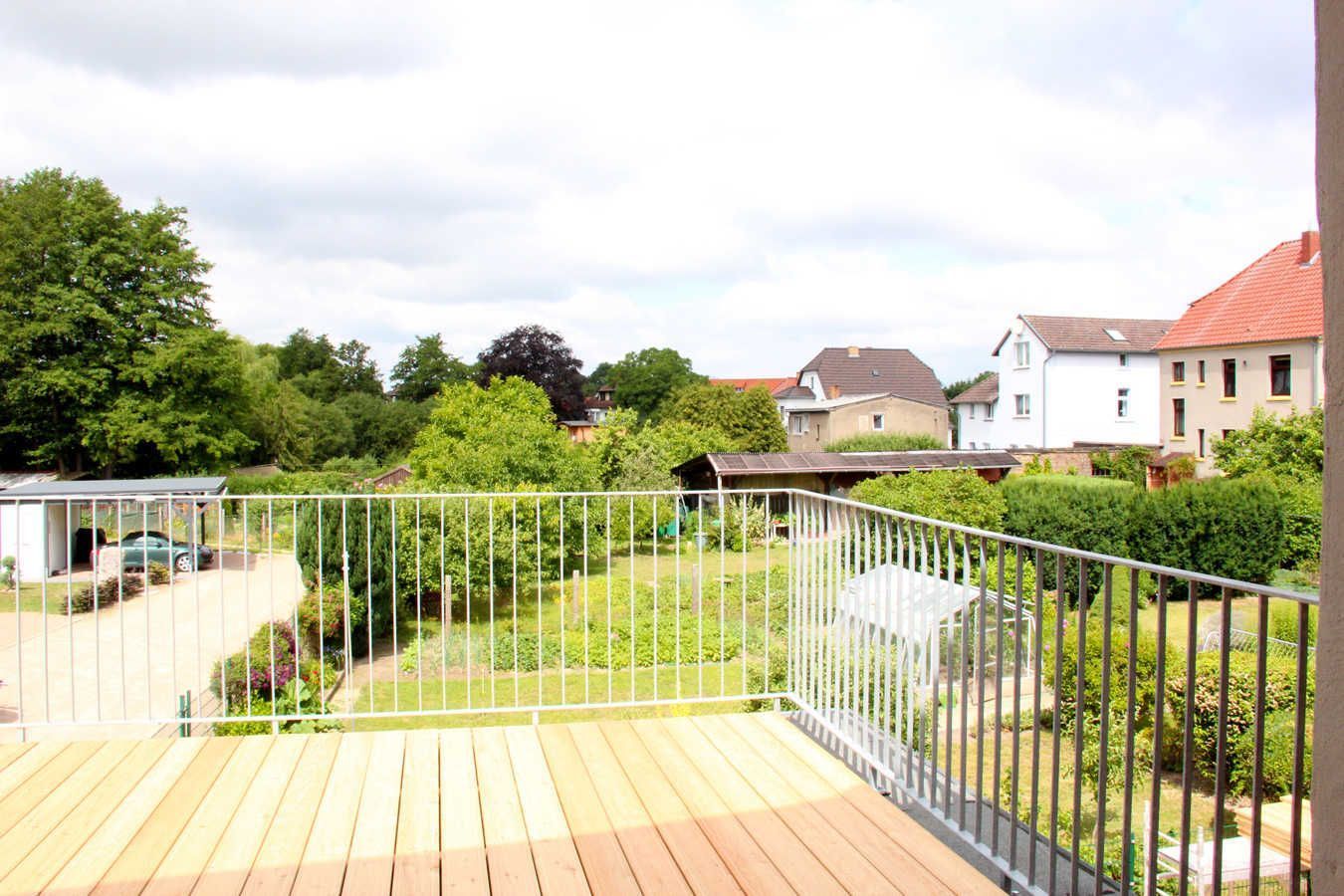 Ein Wohngebiet mit einer Holzterrasse, einem Metallzaun und Häusern im Hintergrund.