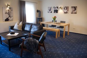 A modern living room with a black leather sofa, a wooden coffee table, a dining table with chairs, and artwork on the walls. - Am Wiesenblick - Müritz apartment (Röbel/Müritz)