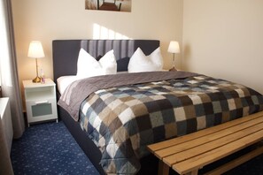 A neatly made bed with a checkered blanket, two bedside lamps, a nightstand with a bottle, and a wooden bench. - Am Wiesenblick - Müritz apartment (Röbel/Müritz)