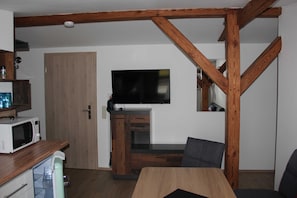 A room with a wooden ceiling, a flat-screen TV mounted on the wall, a microwave on the counter, and a small refrigerator. - Am Wiesenblick - Müritz apartment (Röbel/Müritz)