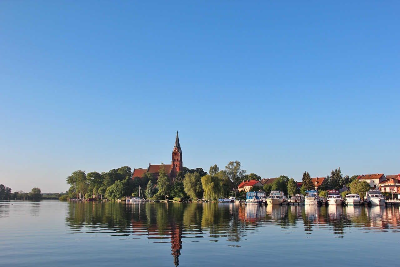 A calm river with boats, a church, and buildings along the shore.
