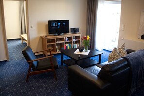 A living room with a TV, bookshelves, a coffee table, and a sofa. - Am Wiesenblick - Müritz apartment (Röbel/Müritz)