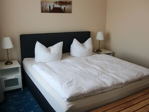 A neatly made bed with white bedding and pillows, two bedside lamps, a small bedside table, and a picture on the wall.